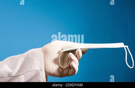 face mask in doctor hand with surgical glove and blue background. Stock Photo