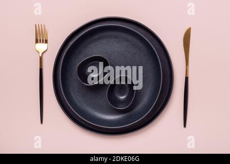 Set of black ceramic plates and cutlery on pastel pink background. Copy space for your text - Image Stock Photo