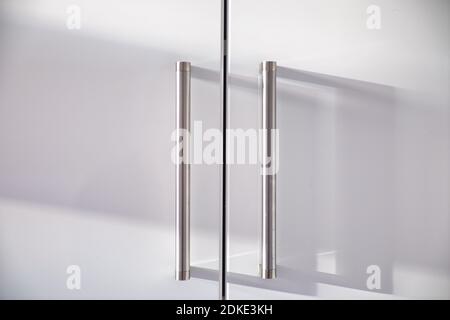 Metal handles on white wooden closet doors with day shadows. Stock Photo