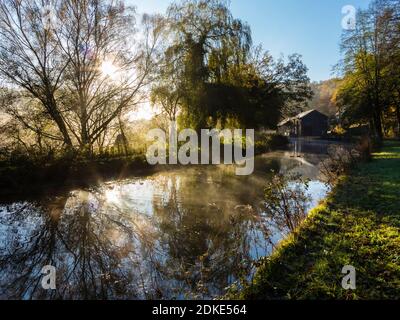 Early morning sunshine streaming through mist and trees on the Cromford Canal in the Derbyshire Peak District England UK Stock Photo