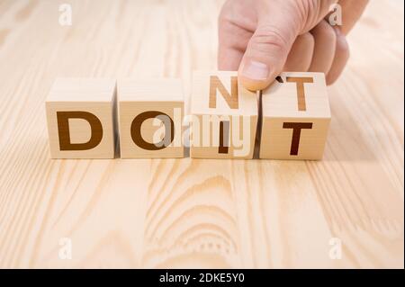 hand flips two cubes with letters, changing the word don't into do it on wooden surface. career growth, taking risk, personal development and motivati Stock Photo