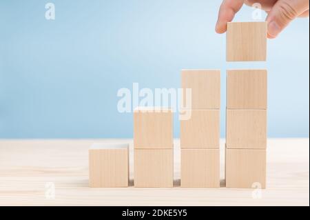 Hands of men arranging blank wood cube block stacking for top staircase shape on wooden table. empty space for your text. Business concept growth succ