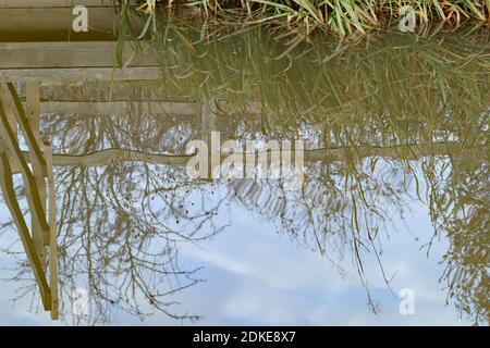 The wavy reflection of clouds and a wooden fence in the murky water of an English canal in autumn Stock Photo