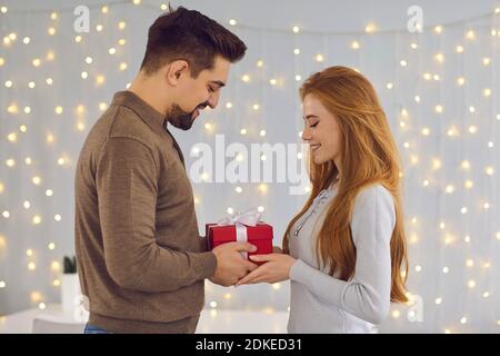 Young happy smiling couple standing and giving presents during celebrating holiday at home Stock Photo