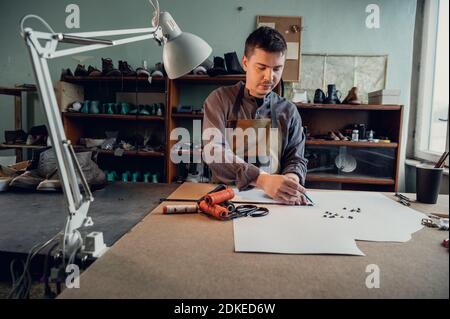 In a family shoe shop a young apprentice works with paper to create a pattern for shoes. Stock Photo