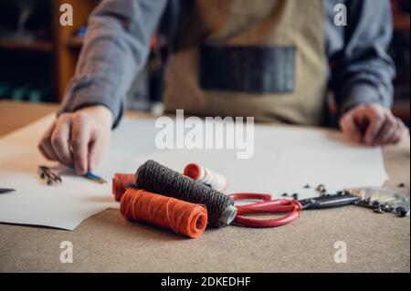 The first stage in the production of shoes is to make an exact pattern from paper, a young shoemaker in uniform at work. Stock Photo