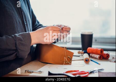 A young shoemaker manually sews decorative elements to leather shoes in the workshop. Stock Photo