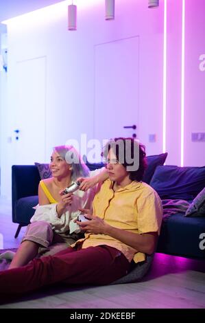 Couple at home playing video games. Girl hug the boy and holding joystick in her hands. Spendning time together at home. Stock Photo