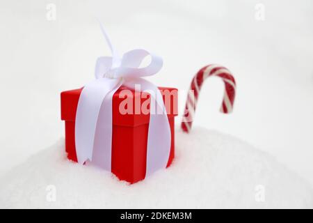 Red gift box with white bow and candy cane on the snow. Romantic present for Christmas or New Year holiday Stock Photo