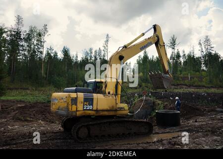 The crawler-mounted power shovel is carrying a concrete ring to install a sewer well in a pipeline at a construction site. Stock Photo