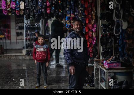 Ariha, Syria. 15th Dec, 2020. A shoe vendor smiles in front of his shop at a local market amid chilly weather conditions. War-torn Syria experiences very hot summers and equally cold winters, which causes major problems for those who were forced into internal displacement. Credit: Anas Alkharboutli/dpa/Alamy Live News Stock Photo