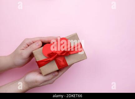 box with gift tied with red ribbon with bow in female hands on pink background Stock Photo