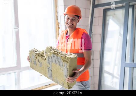 profession, construction and building - happy smiling worker or builder in helmet over room with working equipment at new home or apartment background Stock Photo