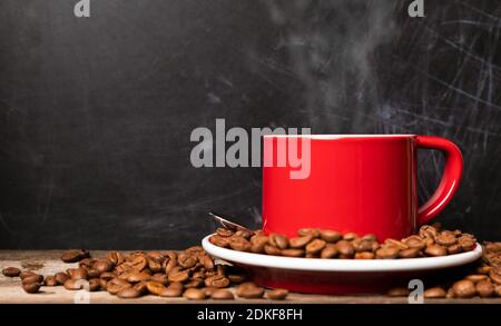 Red cup of coffee with coffee beans on dark textured background. Morning fresh energy concept. Stock Photo