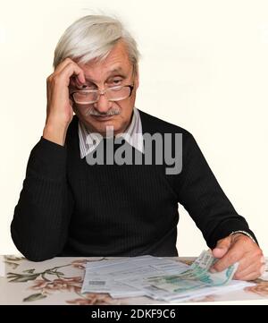 An older man sits at a table in front of him bills and money, he looks at the camera Stock Photo