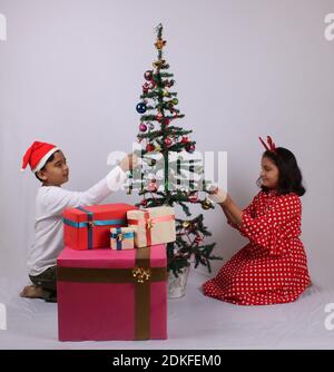 Cute little Indian kids celebrating christmas at home with Santa Hat, Gifts and Xmas Tree Stock Photo