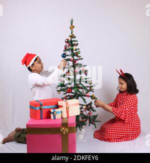 Cute little Indian kids celebrating christmas at home with Santa Hat, Gifts and Xmas Tree Stock Photo