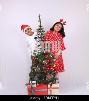 Cute little Indian kids celebrating christmas at home with Santa Hat, Gifts and Xmas Tree Stock Photo