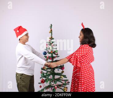 Cute little Indian kids celebrating christmas at home with Santa Hat, Gifts and Xmas Tree Stock Photo