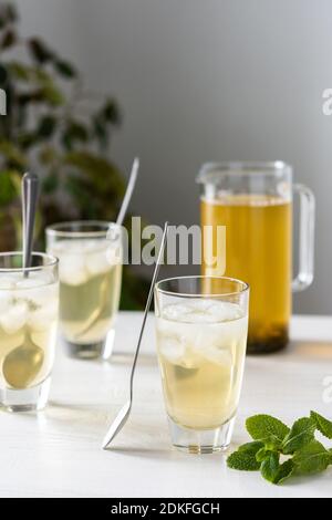 Cold refreshing green tea with ice and mint, tea jug and glasses on white wooden background Stock Photo