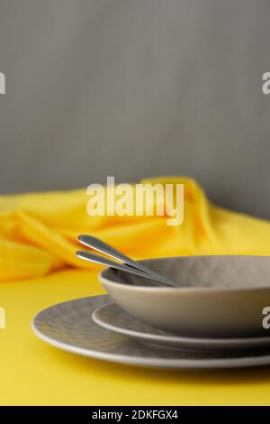 Table setting in trendy colors of the year, gray plates and a fork with a spoon on a yellow background with a yellow tablecloth Stock Photo