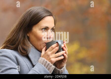 Adult woman drinking coffee standing in a park in autumn contemplating views Stock Photo