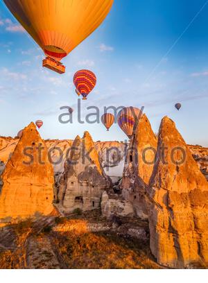 Bright yellow sunrise with colourful balloons floating just above cave homes in Cappodocia