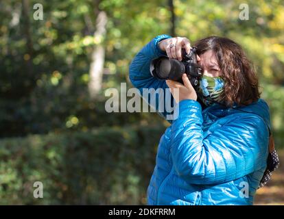 Middle-aged woman wearing a mask takes pictures in nature on an autumn day. Stock Photo