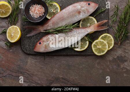 Raw red mullet fish with lemons and herbs on stone background, copy space Stock Photo