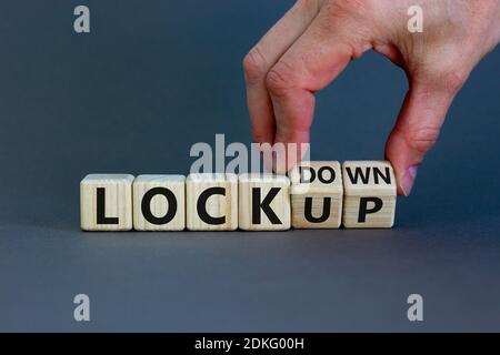 Lockdown or lockup symbol. Hand turns cubes and changes the word 'lockup' to 'lockdown'. Beautiful grey background. Copy space. Business and lockdown Stock Photo
