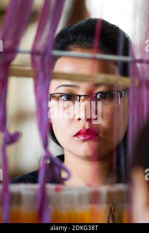 Gangtok, Sikkim, India - Dec 21, 2011: Charming pensive dark-haired Indian woman with eye-glasses working at the loom on Dec 21, Gangtok, Sikkim, Indi Stock Photo