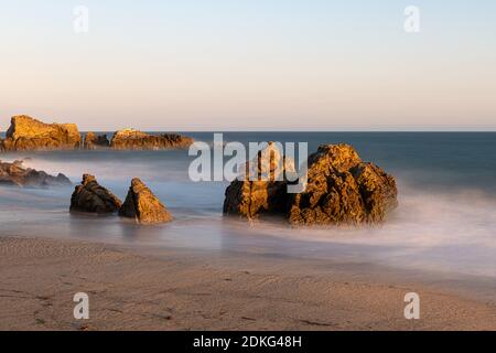 Stunning long-exposure view of smooth waves crashing into rock formations at sunset, Sequit Point, Leo Carrillo State Beach, Malibu, California Stock Photo