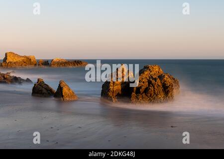 Stunning long-exposure view of smooth waves crashing into rock formations at sunset, Sequit Point, Leo Carrillo State Beach, Malibu, California Stock Photo