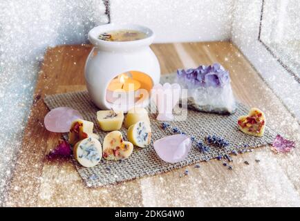 Homemade mini wax melts in aromatherapy lamp diffuser at home interior with rose quartz crystal hearts and angel for decoration on wooden window. Stock Photo