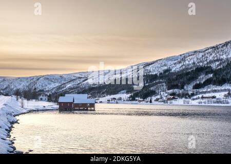 Red wooden house in the wintry, snow-covered landscape by the fjord in Northern Norway / Troms Province