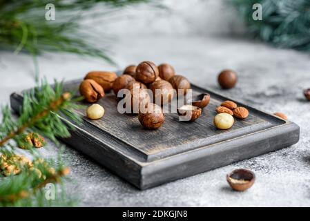 Several types of nuts against the background of spruce branches on a wooden cutting board on a light concrete background Stock Photo