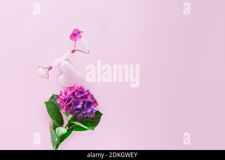 Balanced composition with pink jade roller face massager, and gouache scraper on hydrangea flower on the pink background. Rose quartz. Anti age Stock Photo