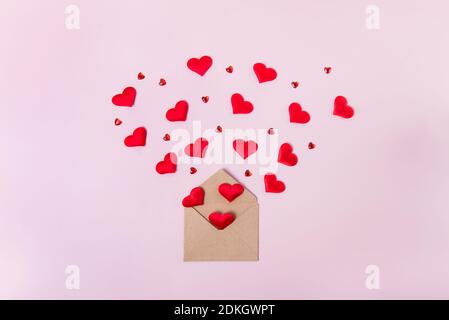 Red hearts fly out of craft paper envelope on light pink background. Valentine day. love concept. Gift, message for lover. Space for text. Stock Photo