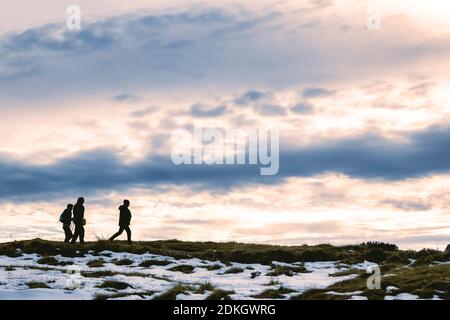 Italy, Trentino, Rolle pass, Dolomites. Hikers in silhouette walk on a grassy ridge at sunset Stock Photo