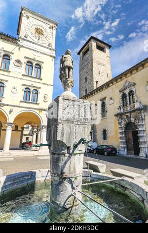 Italy, Veneto, Belluno, Dolomites, the statue of St. Gioatà on the fountain in Piazza del Duomo between the Palazzo dei Rettori with the clock tower and Palazzo dei Vescovi Stock Photo