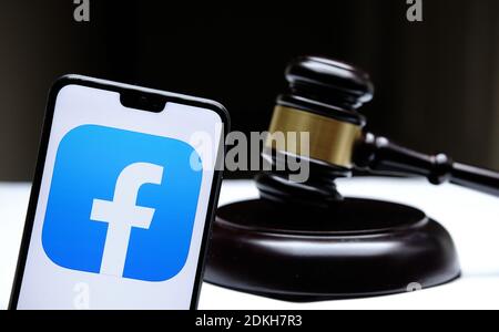 Stafford, United Kingdom - December 15 2020: Facebook logo seen on the smartphone placed next to the judges gavel. Concept for a lawsuit, legal case, Stock Photo