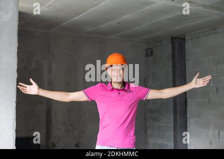 profession, construction and building - happy smiling worker or builder in helmet over room with working equipment at new home or apartment background Stock Photo