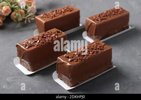 Four mousse desserts covered with chocolate on a dark gray background. Closeup. Stock Photo