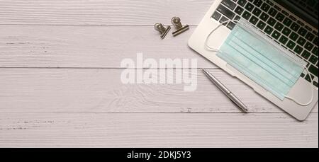 Wood office desk table with laptop, face mask and supplies. Copy space. Stock Photo