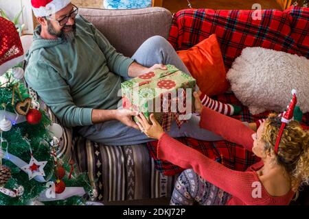 Gifts share and giving action at home with happy adult couple in happy christmas holiday eve day together - red colors and love for cheerful caucasian man and woman enjoying home together during holidays Stock Photo