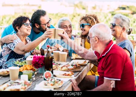 Group of caucasian family people enjoy and celebrate together in outdoor at home with country side green nature view in backgorund - senior and young friends enjoying with food and drinks Stock Photo