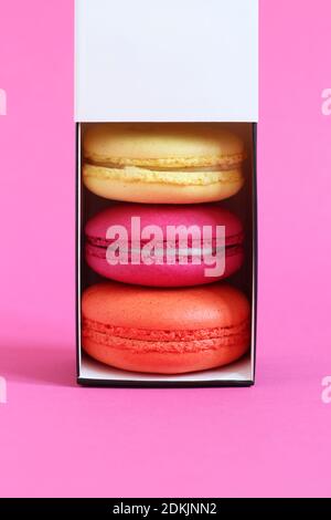 Multicolored macarons in a cardboard box with an open lid standing upright on a pink background. Closeup Stock Photo