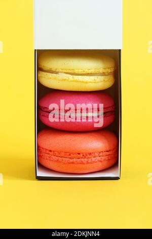 Multicolored macarons in a cardboard box with an open lid standing upright on a yellow background. Closeup Stock Photo