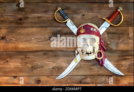 Jolly pirate scull in bandanna with crossed swords and golden teeth on wooden background. Stock Photo