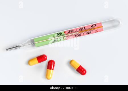 Mercury thermometer and three yellow-red capsules with medicine on a white background Stock Photo